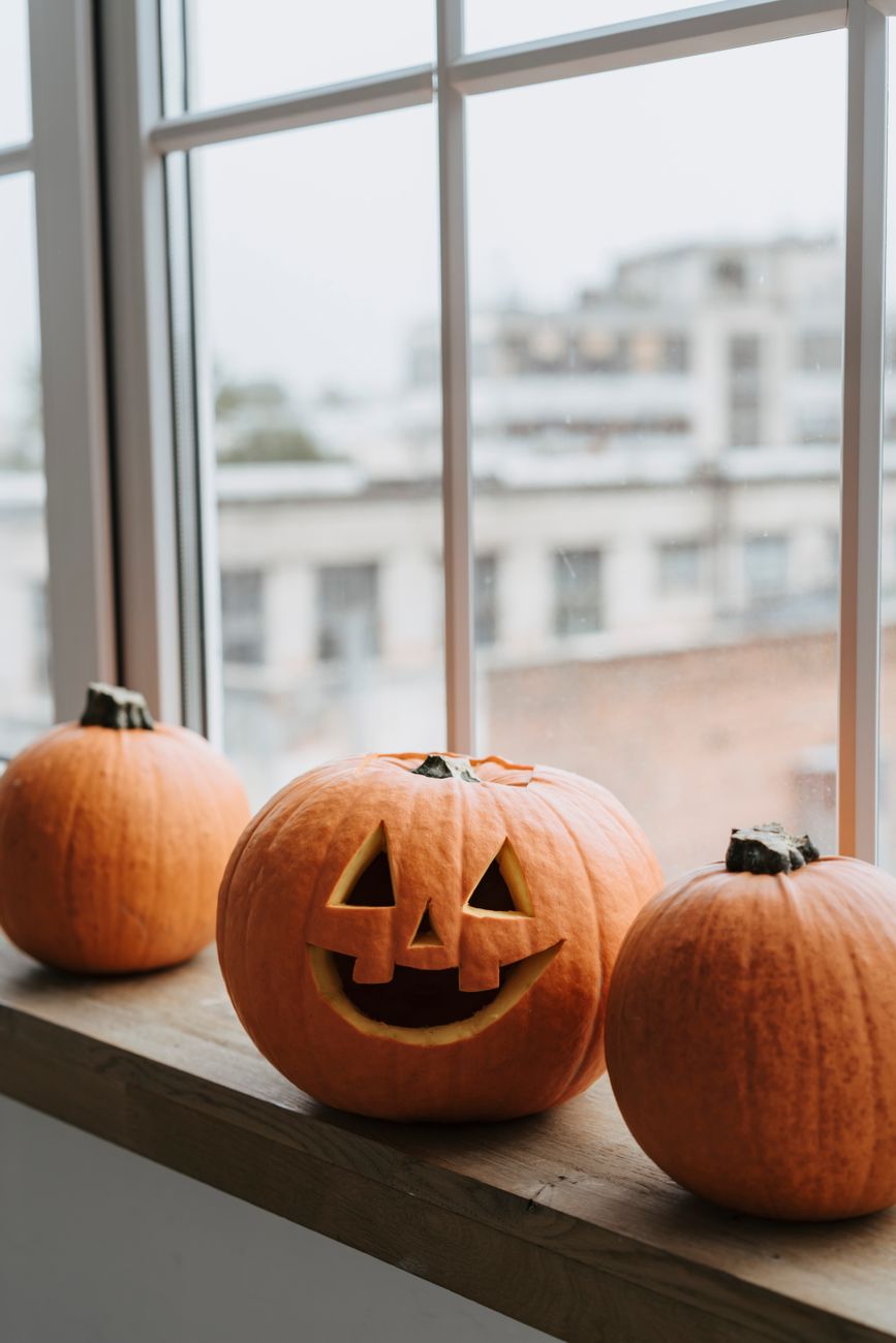 A carved jack-o’-lantern with pumpkins beside a window